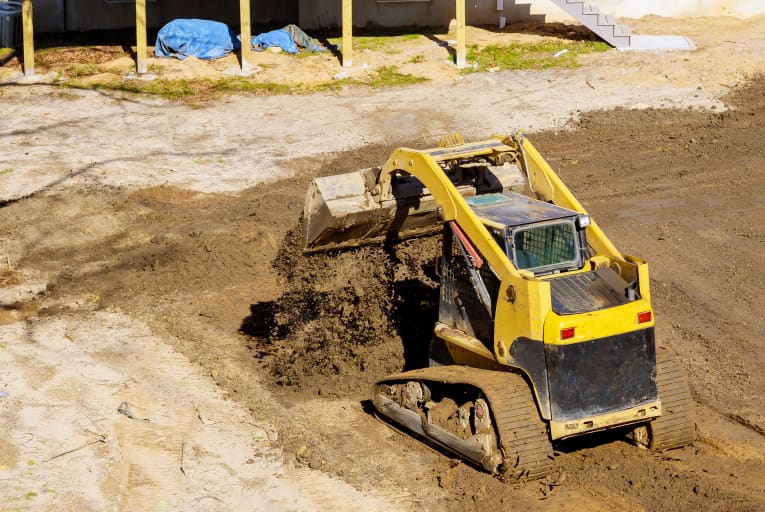 Skid steer on construction site dumping dirt with bucket attachment