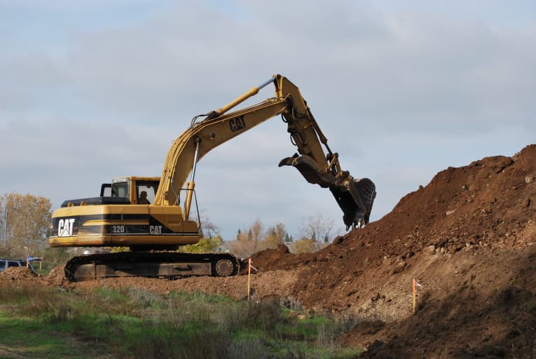A yellow excavator digging from a dirt pile